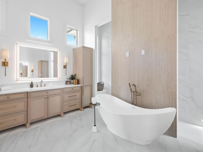 Luxury Bathroom with Wood Cabinets and Double Sinks A luxurious bathroom featuring dark wood vanity cabinets with silver handles and a white marble countertop. The vanity includes two undermount sinks with modern silver faucets. Above the sinks are two rectangular mirrors framed in matching dark wood, accompanied by sleek wall-mounted light fixtures. The walls are painted in a soft neutral tone, complementing the rich cabinetry and creating an elegant, serene atmosphere.